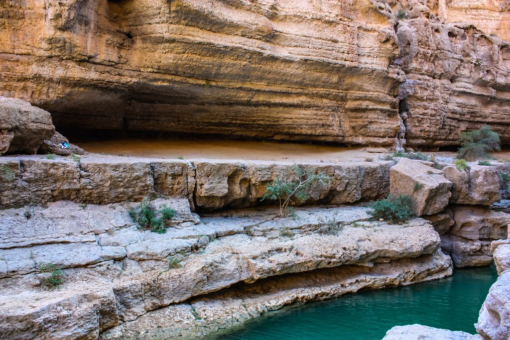 A green pool below sandstone cliffs in Wadi Shab, Oman