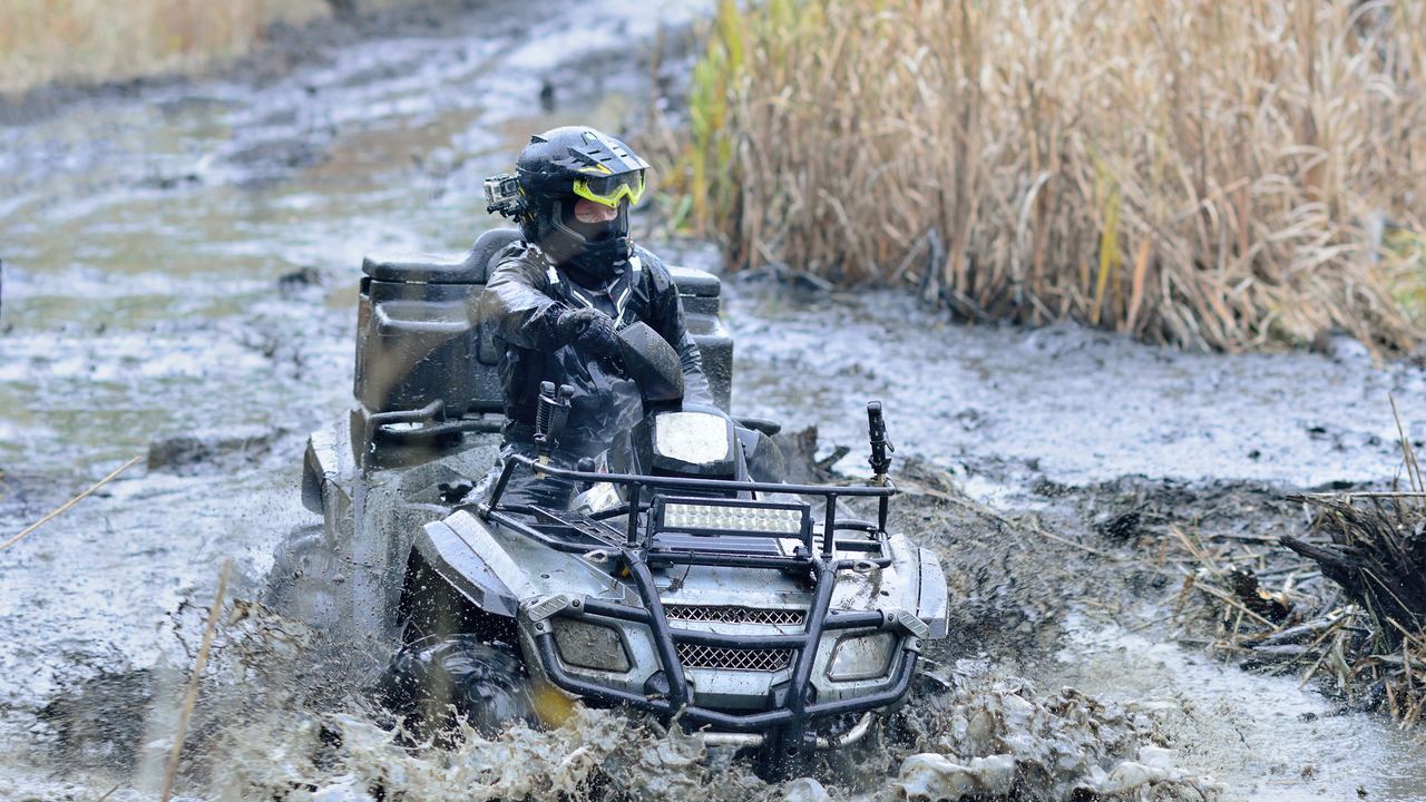 Rider on a quad bike pushing through a muddy, water-filled trail