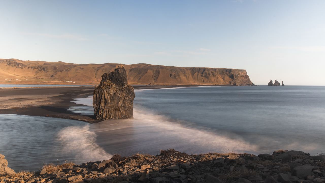 Black sand beach with a basalt sea stack and the Dyrhólaey cliffs under a clear sky