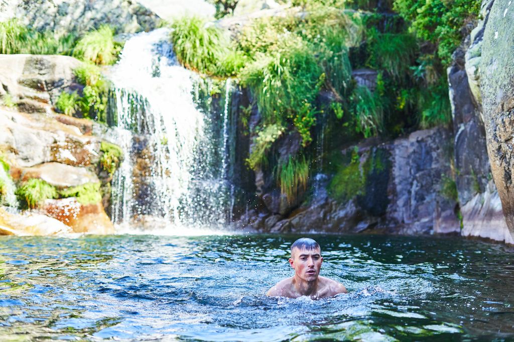 Swimmer in a blue rock pool below a small waterfall among ferns