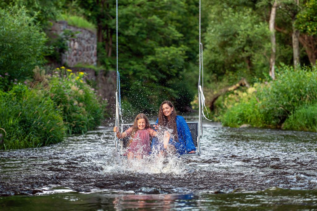 Woman and girl laughing on a rope swing over a shallow forest river