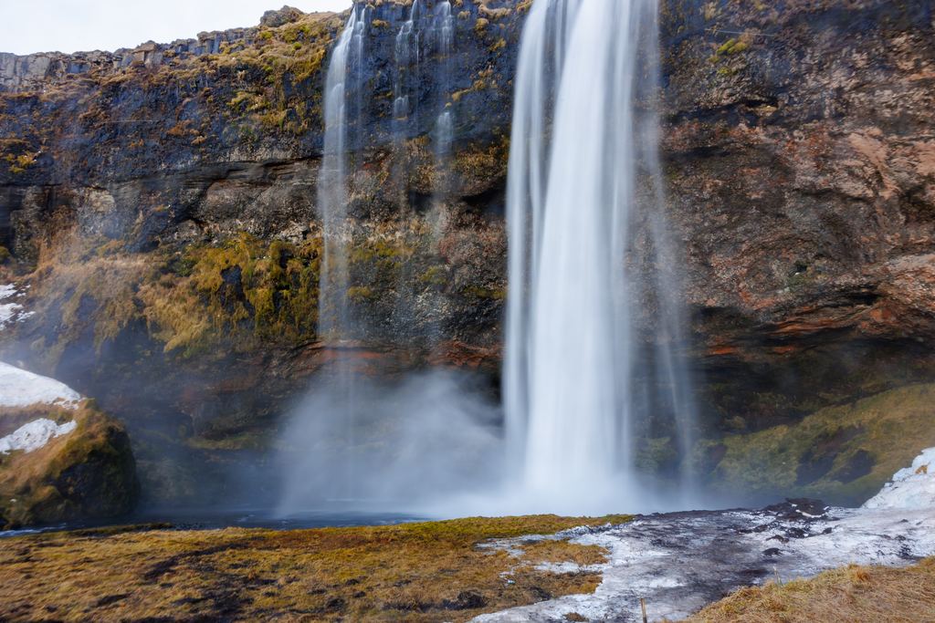 Seljalandsfoss in South Iceland falling over a dark cliff with moss and mist at its base