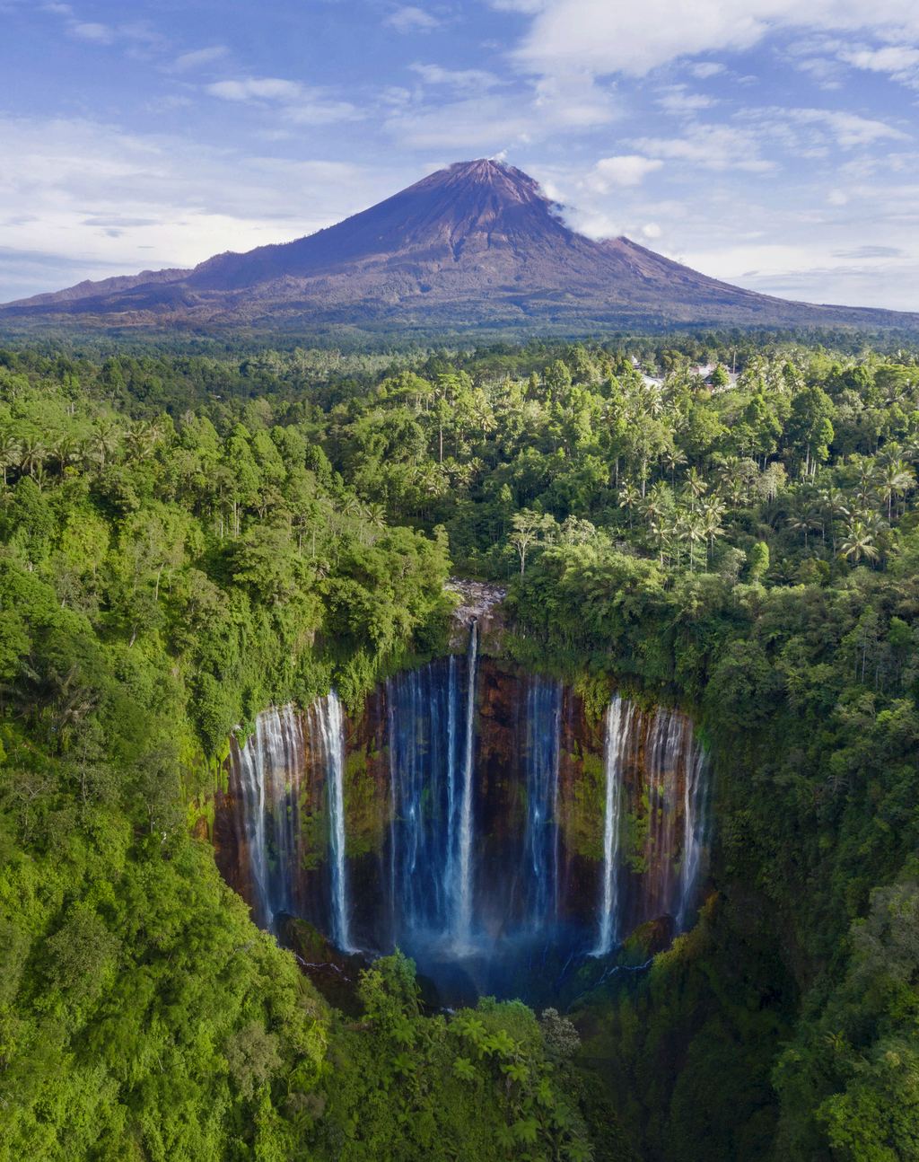 Mount Semeru rising above forest and the curtain of Tumpak Sewu waterfall in East Java