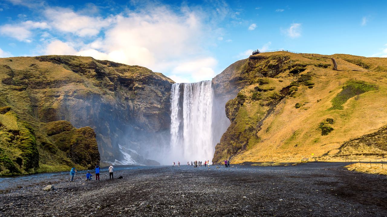 Skógafoss waterfall with visitors on the black gravel in front of the cliff