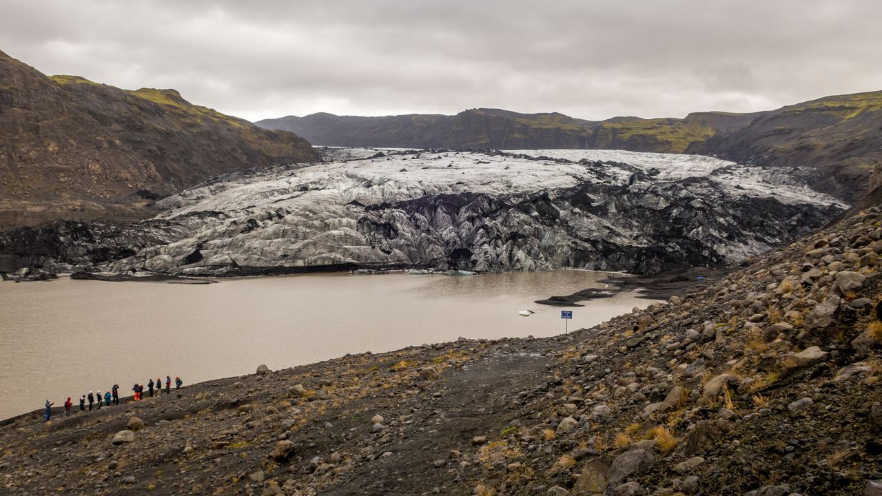 A line of hikers on the shore of the glacial lagoon below the Sólheimajökull ice tongue