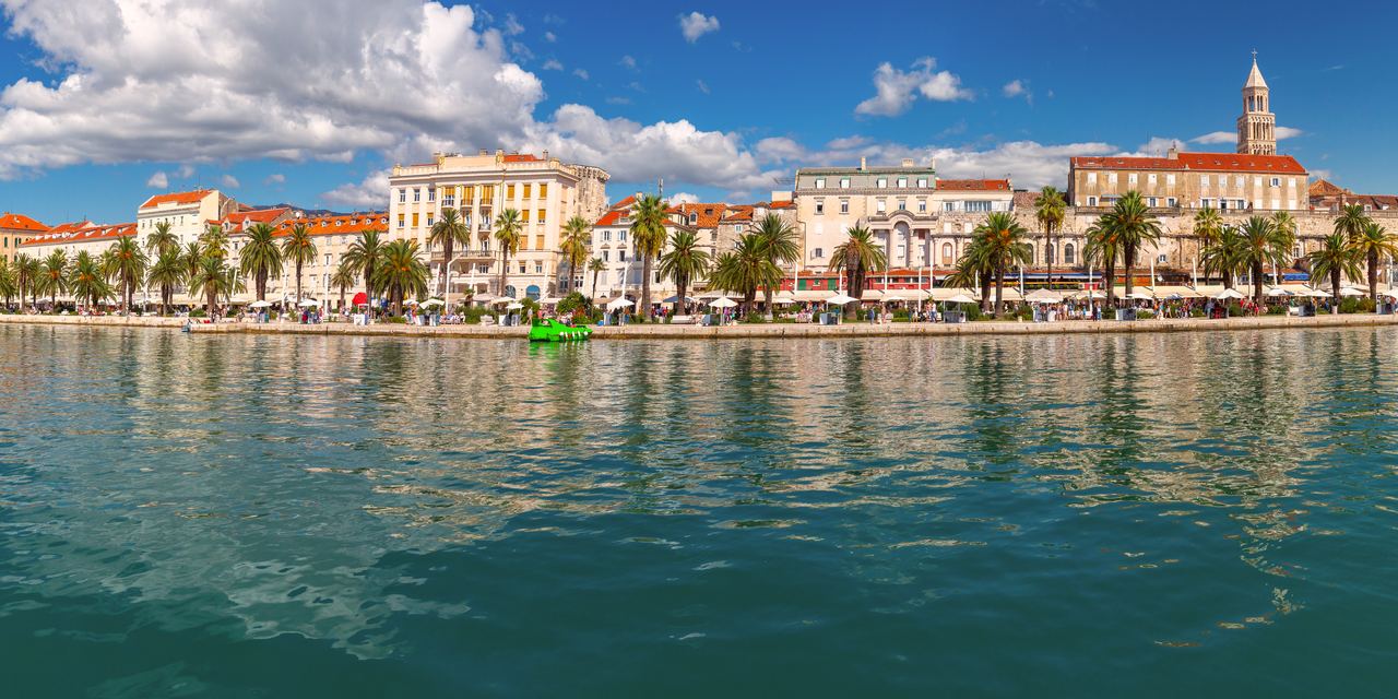 Palm-lined Riva waterfront promenade in Split, Croatia, with the bell tower above the buildings