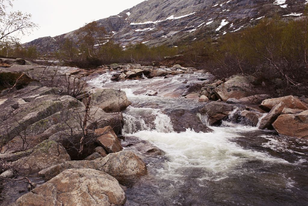 A stream running white over boulders below a rocky slope with patches of snow