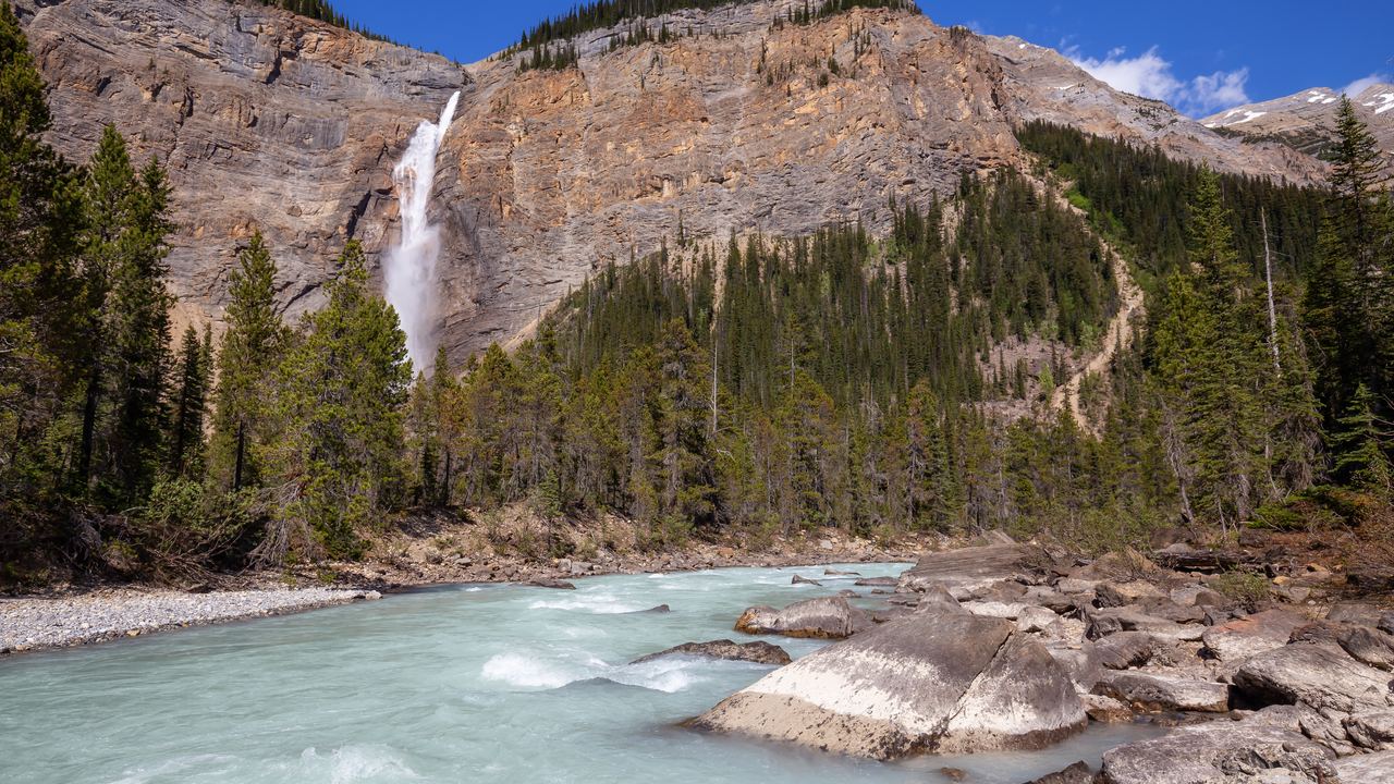 Takakkaw Falls dropping down a cliff above a turquoise glacial river in Yoho National Park, Canada