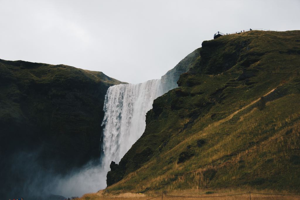 A tall waterfall dropping over a green cliff under an overcast sky