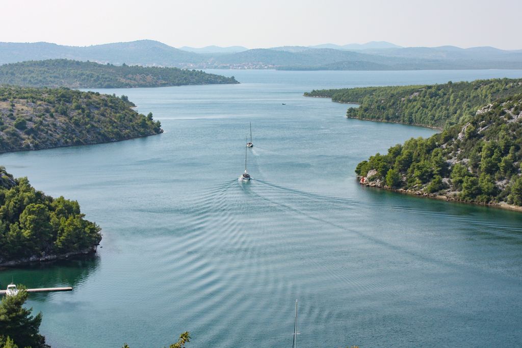 Sailing boats on a wide channel of the Krka River between wooded hills, Krka National Park, Croatia