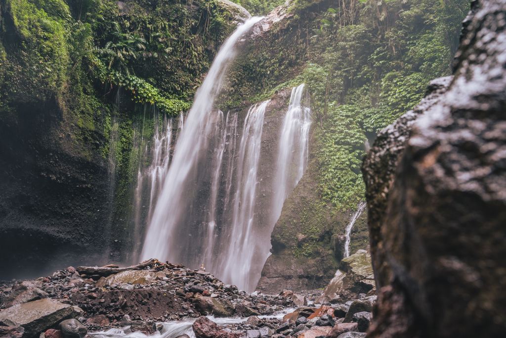 Tiu Kelep Waterfall on Lombok, water spreading over mossy rock above a boulder field