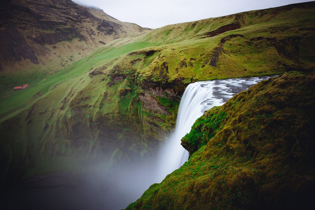 The edge of Skógafoss seen from above with mist and green slopes below