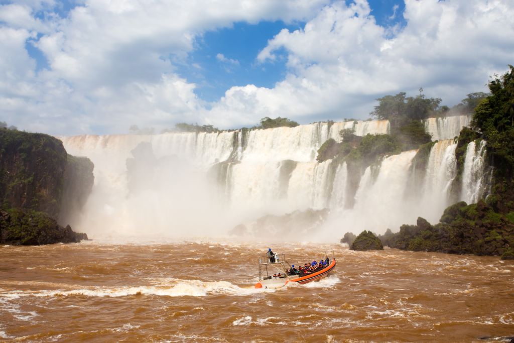 Orange tourist boat with passengers on the brown river in front of the Iguazu Falls
