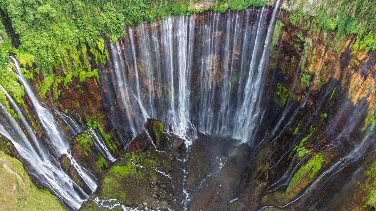 Aerial view of the Tumpak Sewu waterfall pouring over a horseshoe cliff into a green gorge