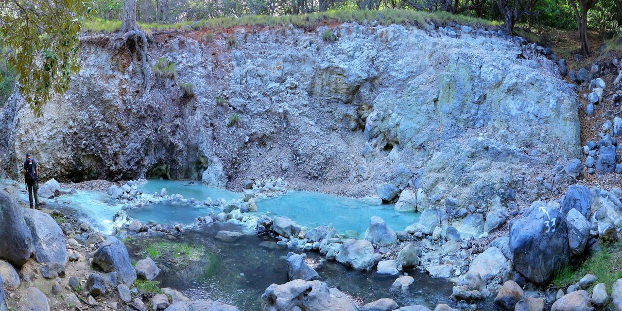 Turquoise stream below pale volcanic rock with hikers, Rincón de la Vieja National Park, Costa Rica
