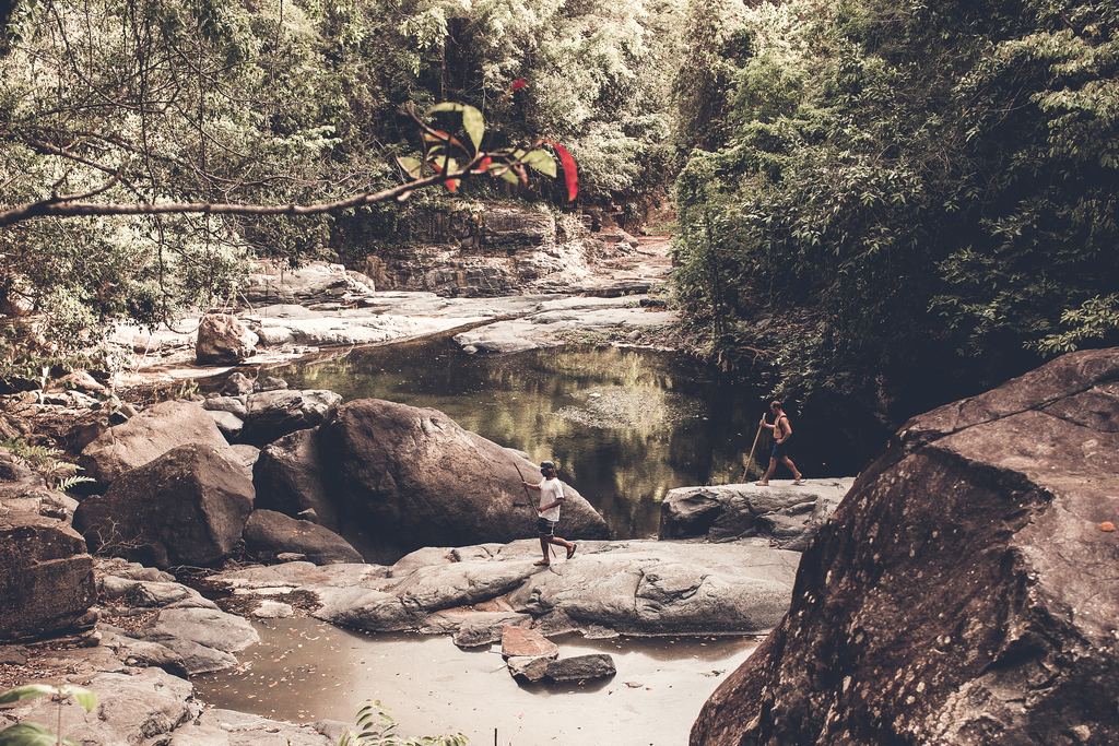 Two people on large rocks beside a clear pool in a forest stream