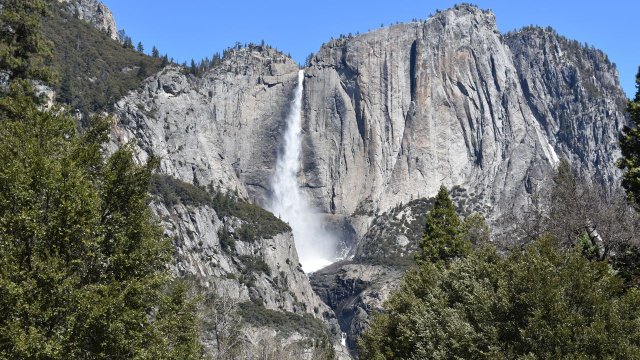 Upper Yosemite Fall dropping down a granite cliff in Yosemite National Park, California, under a blue sky