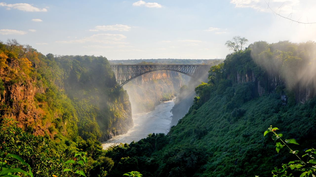 Victoria Falls Bridge spanning the Zambezi gorge in soft light, with mist rising from the gorge
