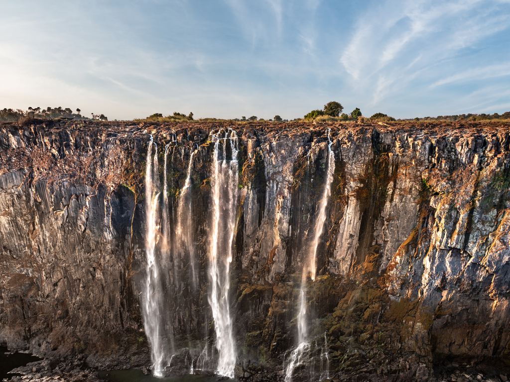 Water falling in thin streams down a dark basalt wall at Victoria Falls under a clear sky