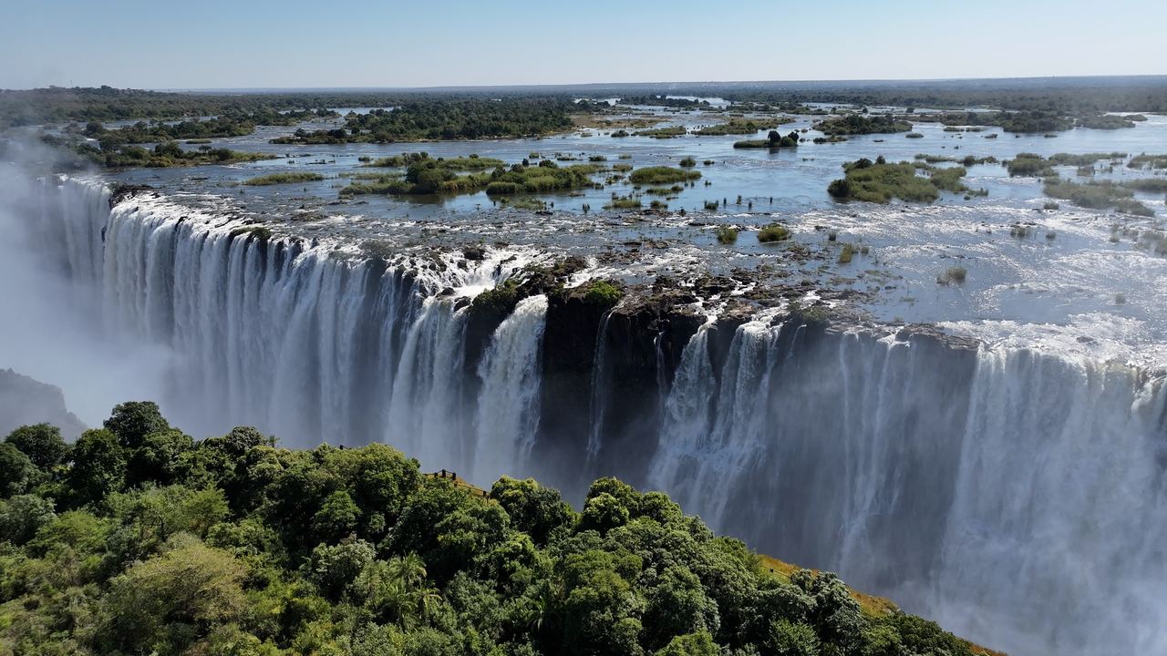 The wide front of Victoria Falls on the Zambezi with islands above the edge and forest in the foreground