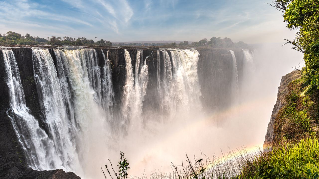 Victoria Falls seen from the Zimbabwe side, with a faint rainbow in the spray below the wall of water
