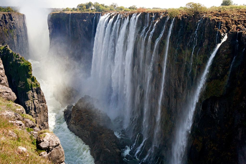 Victoria Falls seen from a cliff-top viewpoint, with spray and a faint rainbow over the gorge