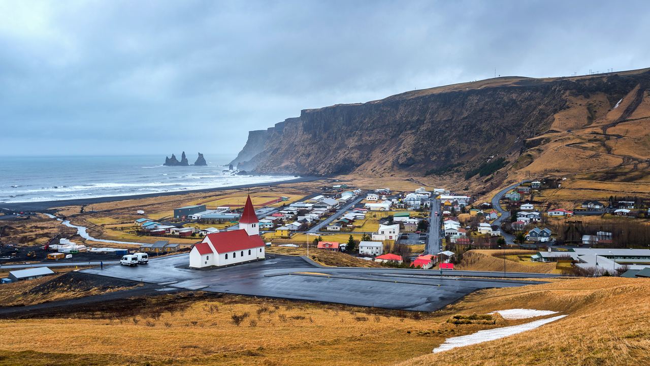 The red-roofed church in Vík with the village below the cliffs and sea stacks offshore