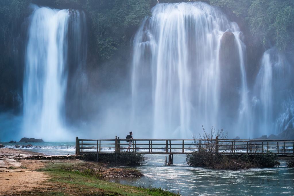 A visitor stands on a footbridge in front of the tall falls of Ban Gioc in Cao Bang