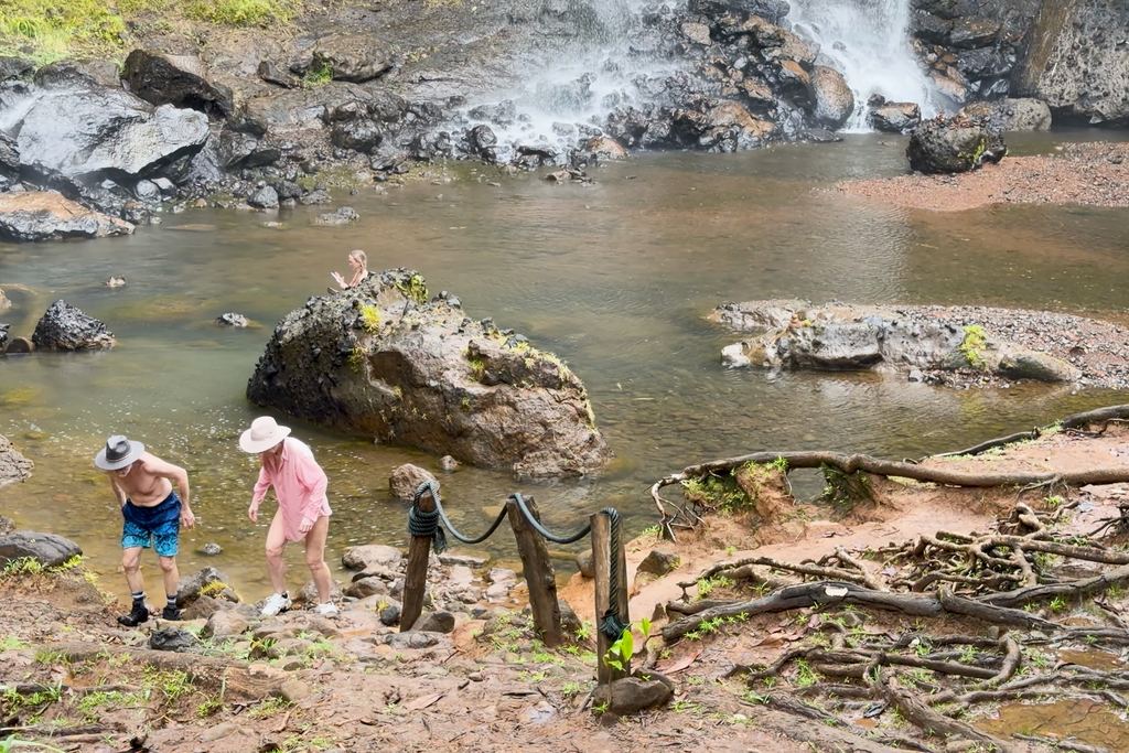 Visitors walking over wet rock and tree roots at the base of a waterfall in the forest