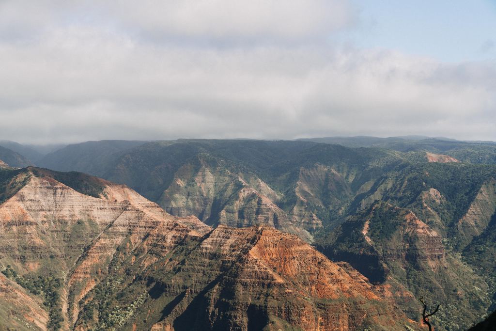 Red and green ridges of Waimea Canyon on Kauai, Hawaii, under a cloudy sky