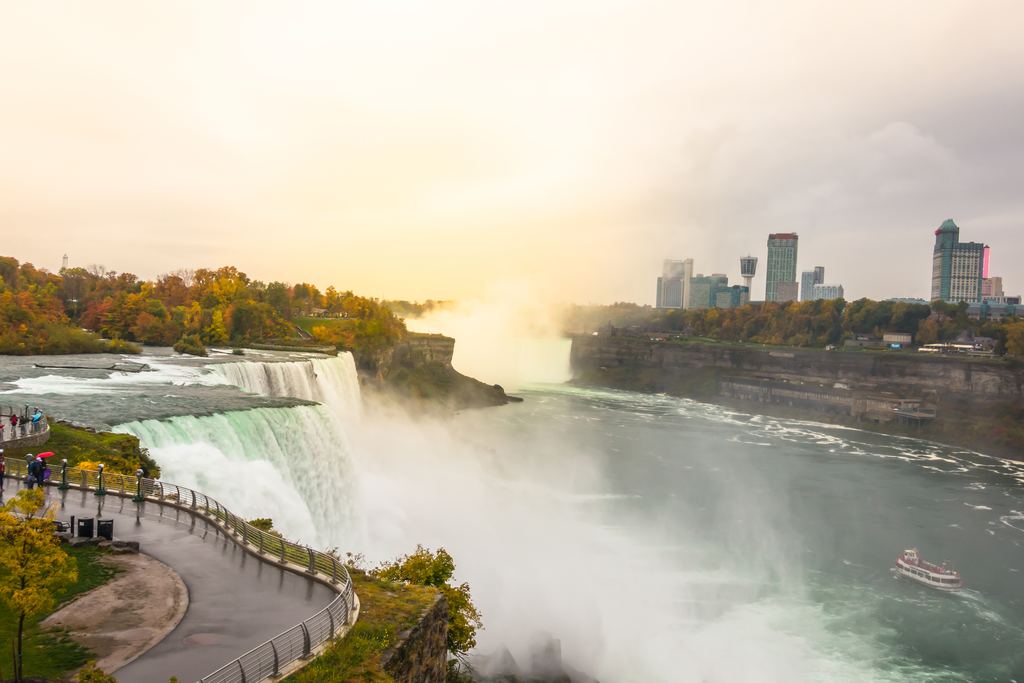 Walkway beside the American Falls in Niagara Falls State Park at sunrise, with autumn trees