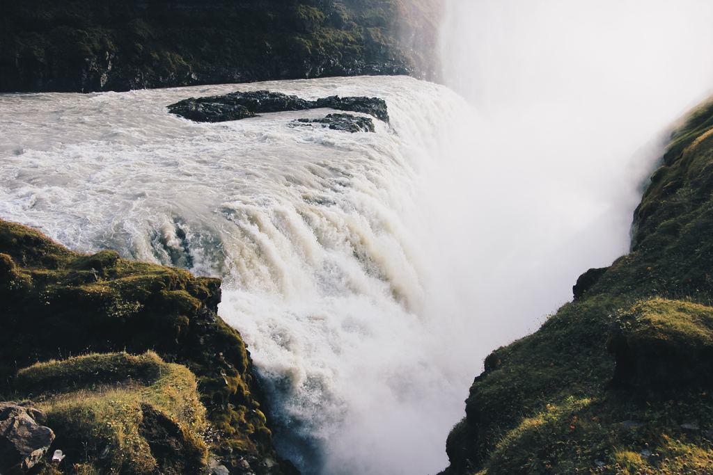 Water running to the lip of a waterfall and into a mist-filled drop between mossy rock walls