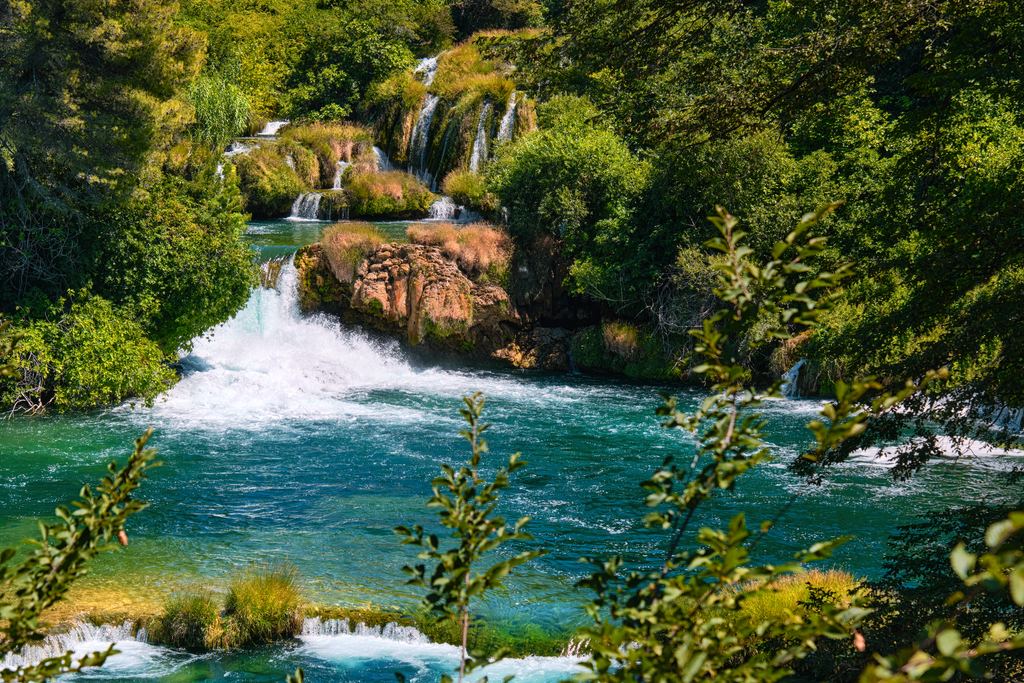 Turquoise water below Skradinski buk framed by green leaves, Krka National Park, Croatia
