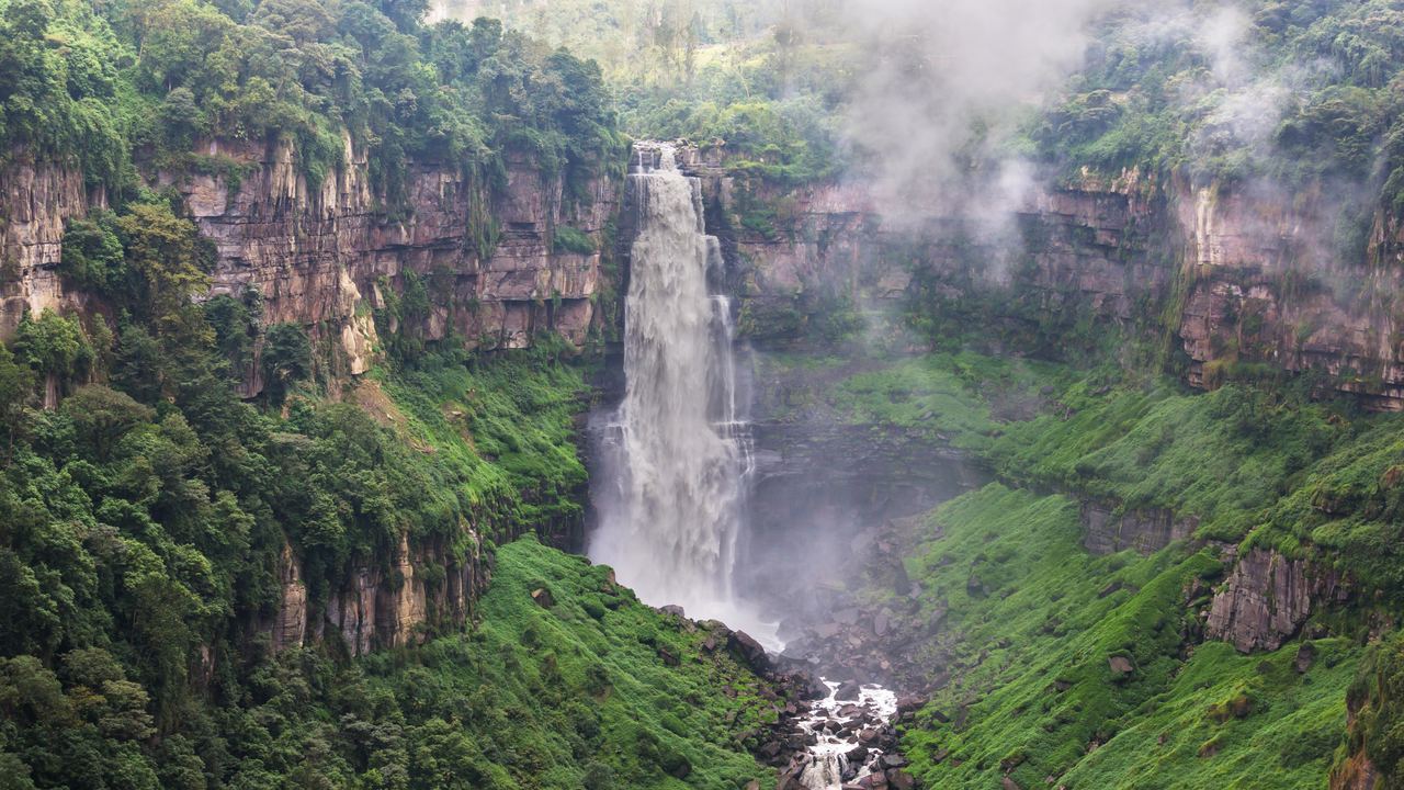 Tall waterfall dropping into a misty forested canyon in Colombia