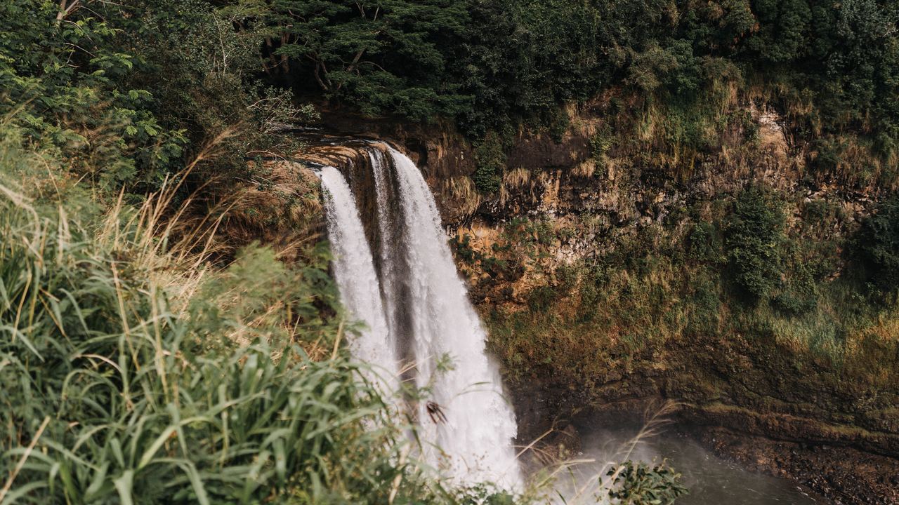 A two-stream waterfall in Wailua River State Park on Kauai, Hawaii, surrounded by tall grass