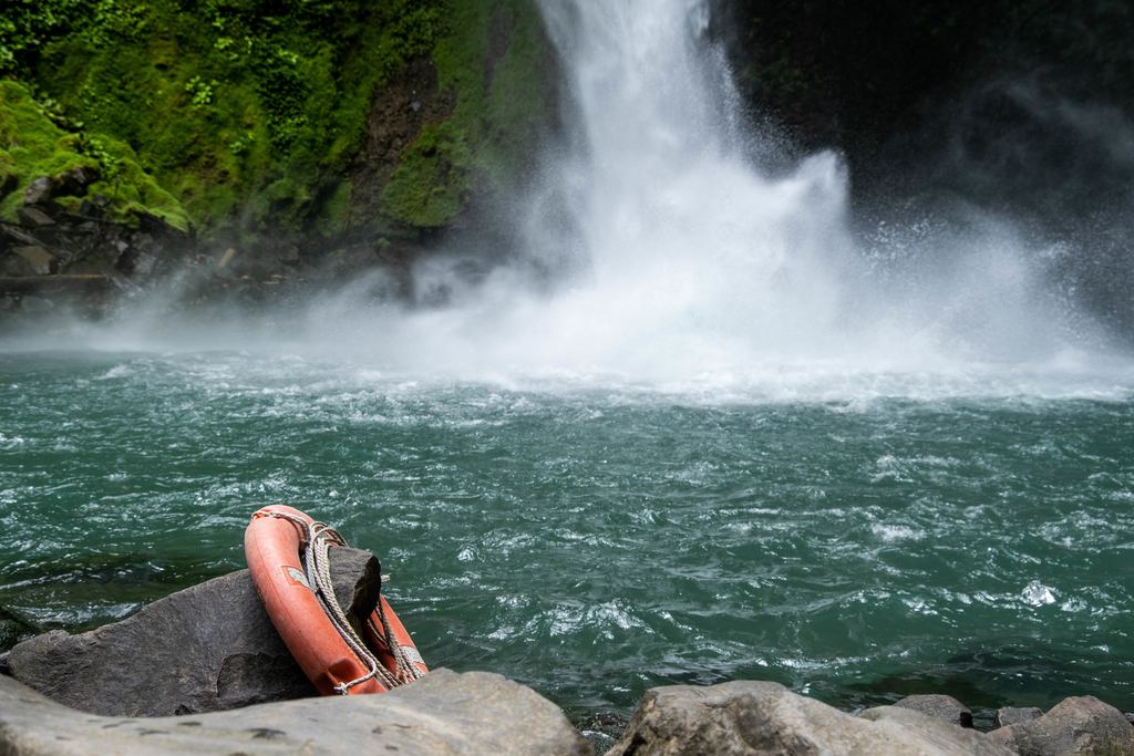Orange lifebuoy hanging on a rock beside a waterfall pool with green water