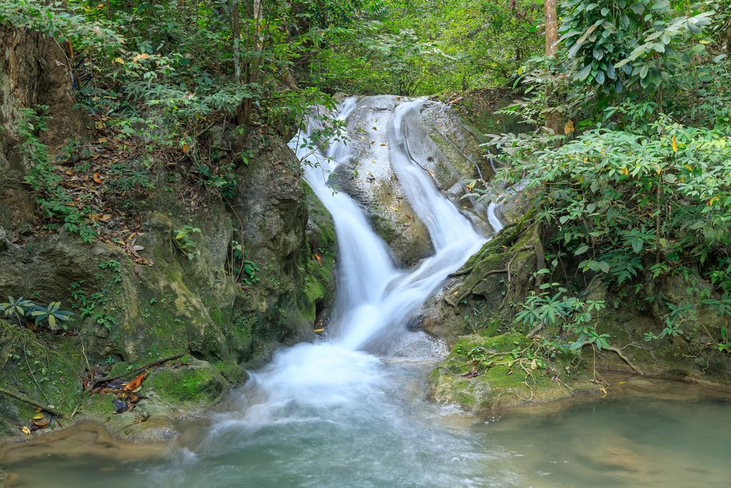 A small waterfall over mossy rock in a forest at Erawan National Park, Thailand