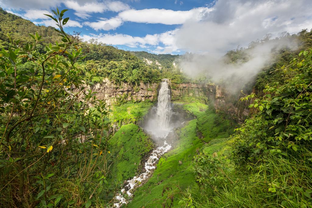 Waterfall falling from a rock rim into a green canyon under a blue sky in Colombia