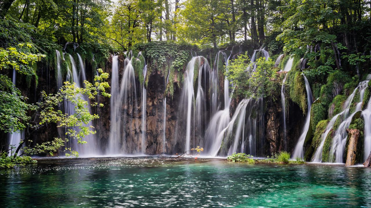 Several waterfalls falling over a rock wall into a turquoise lake at Plitvice Lakes National Park, Croatia